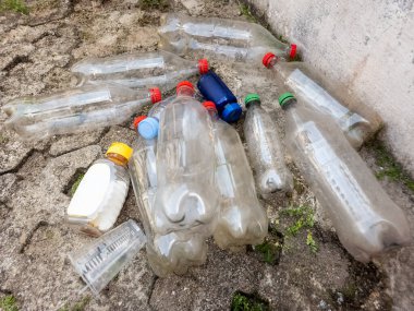 Yukarıdan çekilen bir fotoğraf, kaba ve çatlak bir yüzeye saçılmış plastik şişe ve konteynır koleksiyonunu gösteriyor. Görüntü, plastiğin çevre üzerindeki etkisine odaklanarak atık ve çevre kirliliği sorununu vurguluyor. Şey...