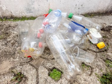Çöpe atılmış plastik su şişeleri ve diğer plastik atıklar beton bir yüzey üzerinde yer alıyor. Bu da çöp atma veya uygun olmayan atık bertaraf etme olasılığını gösteriyor. Görüntü, plastik kirliliğinin çevresel etkilerini gösteriyor.