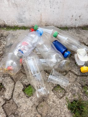 Beton bir yüzeyde atılmış plastik şişeler ve diğer plastik atıkları gösteren yakın plan bir çekim. Görüntü kirlilik ve çevresel bozulma sorununu vurguluyor ve çeşitli plastik kaplar içeriyor. Sahne 