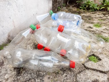 Hurdaya çıkmış plastik şişeler beton bir yüzeyde yatıyor ve plastik atık sorununu vurguluyor. Renkli kapaklı berrak şişeler, kirlilik ve geri dönüşüm ihtiyacını vurgulayarak dağıtıldı. Resim bir ileti iletir 
