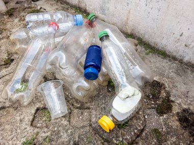 Çöpe atılmış plastik şişeler ve plastik bardaklar kaba beton bir yüzeye saçılmıştır. Renkli kapaklı temiz plastik şişelerin çeşitli boyutları ve şekilleri birbirine karıştırılır. Görüntü çevre kirliliğini ve sorunu vurguluyor