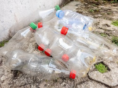 Renkli kapaklı şeffaf, boş plastik su şişeleri koleksiyonu yıpranmış beton bir yüzeye atılmış. Şişeler şekil ve boyut olarak değişir, bazı kullanım belirtileri gösterir. Görüntü, plastik atık ve çevresi sorununu vurguluyor