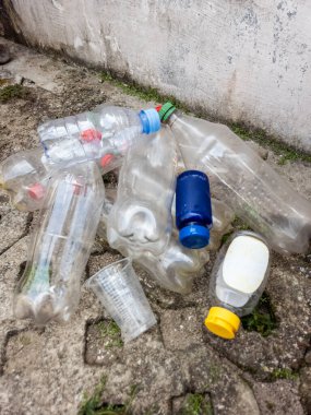 Çevresel kirlilik ve atık sahnesini tasvir eden boş plastik şişeler ve plastik bardaklar kaba beton bir yüzeye saçılmıştır. Görüntü, plastik atık sorununu ve çevre üzerindeki etkisini vurguluyor. Bileşim.