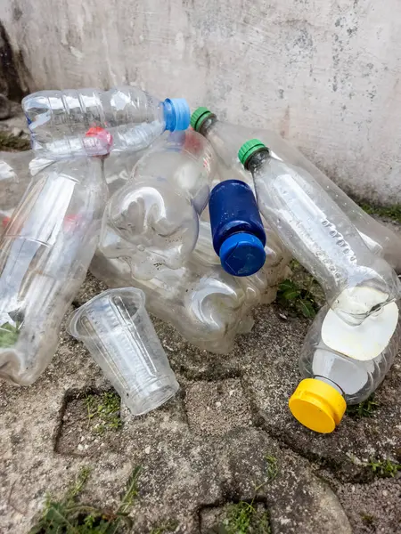 Çöpe atılmış plastik şişeler ve plastik bardaklardan oluşan bir koleksiyon, çevresel plastik atık sorununu betimleyen beton bir yüzeye saçılmış durumda. Görüntü, atıkların uygun olmayan şekilde atılmasının yol açtığı kirlilik sorununu vurguluyor. Şişeler geliyor. 