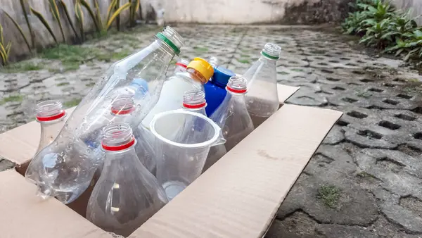 Geri dönüşüme hazır çeşitli plastik şişeler ve kaplarla dolu bir karton kutu. Görüntü, atık yönetimi ve çevresel sorumluluğun önemini vurguluyor. Şişeler farklı şekillerde, boyutlarda ve renklerde.