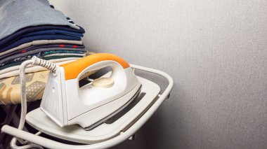 Yakın plan çekimde ütülü bir ütü masası ve düzgünce istiflenmiş giysiler sergilenir. Sahne içeride, düz bir duvarın yanında, ev ortamını ön plana çıkarıyor. Görüntü, organize olmuş bir aile ortamını yakalıyor.