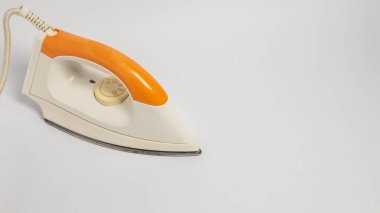 Turuncu saplı ve krem rengi vücutlu elektrikli ütünün yakın çekim çekimi, temiz beyaz arka plana ayarlanmış. Ütü çapraz olarak konumlandırılır, tasarımı ve özellikleri sergilenir. Kordon görünür durumda. Görüntü iyi aydınlatılmış ve suita