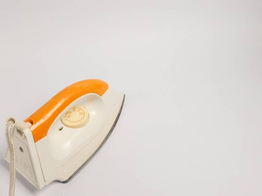 Elektrikli ütünün yakın çekim stüdyosu. Ütü öncelikle beyaz ve sapında turuncu aksanlar var. Çaprazlama olarak düz beyaz bir arkaplanda, temiz ve minimalist bir kompozisyon oluşturuyor. Resim tasarım ve şekli vurgular 