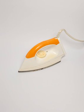 Temiz beyaz arka planda izole edilmiş retro-stil elektrikli ütünün yukarıdan aşağı görüntüsü. Ütünün krem renkli bir vücudu parlak turuncu bir sapı ve ısı kontrol kadranı var. Kordon görünür durumda. Kompozisyon basit ve odaklı, bunu vurguluyor