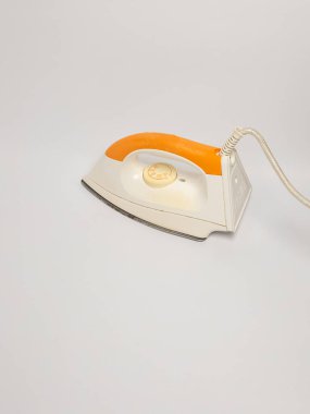 Bu görüntüde turuncu saplı ve beyaz gövdeli klasik bir elektrikli ütü gösteriliyor. Ütü, tasarımı ve özellikleri hakkında net bir görüşe olanak sağlayan bir açıyla konumlandırılmıştır. Tarafsız arkaplan,