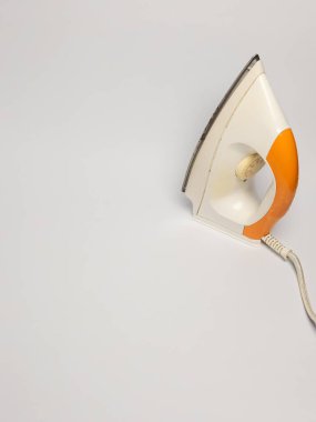 Turuncu saplı eski bir elektrikli ütünün yukarıdan aşağı vuruşu, temiz beyaz arka plana ayarlı. Görüntü ütünün tasarımını ön plana çıkarıyor ve yıpranma ve yıpranmayı gösteriyor. Kompozisyon basit, nesneye odaklanma. Aydınlatma eşit ve açılı.