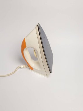 Bu resim, turuncu ve beyaz renkli, temiz beyaz bir yüzey üzerinde dinlenen vintage tarzı bir demire sahiptir. Demir, tasarımını ve taban levhasının dokusunu gösteren bir açıyla konumlandırılmıştır. Kompozisyon basit, vurgulamak için... 