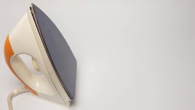 Beyaz arkaplana yerleştirilmiş turuncu ve beyaz renkli bir ev ütüsünün yakın plan görüntüsü. Demir hafifçe açılıdır, tasarımı ve şekli sergilenir. Görüntü iyi ışıklandırılmış ve nötr bir tona sahip, bu da onu çeşitli durumlar için uygun kılıyor. 