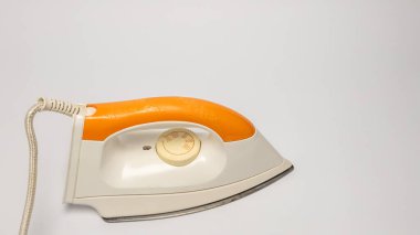 Yakın çekim bir stüdyo çekiminde turuncu sapı ve beyaz gövdesiyle birlikte antika bir elektrikli ütü bulunur. Demir, beyaz bir yüzeye çapraz olarak yerleştirilir ve kordonu görünür olur. Kompozisyon, çizim için uygun tasarım ve ayrıntıları vurgular