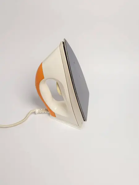 Bu resim, turuncu ve beyaz renkli, temiz beyaz bir yüzey üzerinde dinlenen vintage tarzı bir demire sahiptir. Demir, tasarımını ve taban levhasının dokusunu gösteren bir açıyla konumlandırılmıştır. Kompozisyon basit, vurgulamak için... 