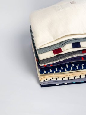 Yakın plan çekimde, çeşitli renk ve desenler sunan düzgünce katlanmış giysiler sergilenir. Çeşitli gömlekler ve diğer kıyafetleri kapsayan etkinlikte moda, düzen ve tertiplik üzerinde duruluyor. Düz arkaplan f 'yi güçlendirir