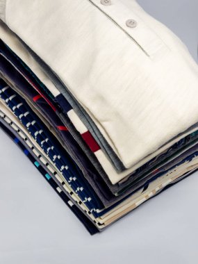 Yakın çekim bir stüdyo sergisi düzgünce dizilmiş katlanmış gömlek yığını. Gömlekler çeşitli renk ve desenlere sahip, çeşitli stilleri gösteriyor. Ürünler düzenli ve düzenli görünüyor, bu da düzen ve temizliğe odaklandığını gösteriyor. - Evet.