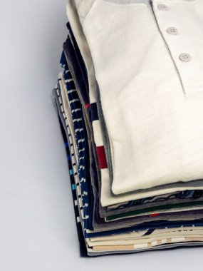 Yakın çekim çekimleri düzgünce dizilmiş günlük gömlekler sergiliyor. Gömlekler çizgiler ve katı renkler de dahil olmak üzere çeşitli renk ve desenler sergiliyor. Kompozisyon, temiz beyaz bir sırtla, giysinin dokusunu ve detaylarını vurgular.