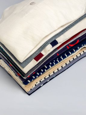 Üst açılı bir fotoğraf, düzgünce düzenlenmiş katlanmış gömlekler sergiliyor. Gömlekler çeşitli renkler, desenler ve dokular sergiliyor. Bu kompozisyon, temiz ve görsel açıdan çekici bir estetik, yaşam tarzı ve moda ile ilgili içerik yaratır.