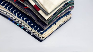 Çeşitli desenlere ve renklere sahip katlanmış gömlek yığınının yakın çekimi. Gömlekler temiz ve düzenli bir görüntü yaratmak için beyaz bir yüzeyde düzgünce düzenlenmiştir. Kompozisyon, giysi parçasının farklı dokularını ve tasarımlarını vurgular