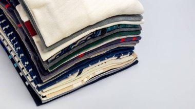 Bir yığın katlanmış kıyafetin yakın plan çekimi, çeşitli renk ve desenler sergiliyor. Kıyafetler düzgünce düzenlenmiş, düzen ve temizliğe işaret ediyor. Tarafsız arkaplan, yaşam tarzı veya yaşam tarzı için uygun tekstil odağı artırır 