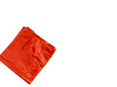 Düz beyaz arka planda katlanmış turuncu plastik bir alışveriş çantasının yukarıdan çekimi. Çantanın dokusu görülebilir ve ışıklandırma onun parlak görünümünü vurguluyor. Kompozisyon basit, nesnenin kendisine ve renginin zıtlığına odaklanıyor.