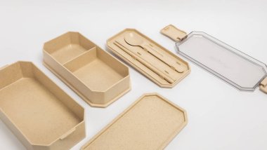 Bir bej bento kutu seti düz beyaz bir arkaplan karşısında sergilenir. Sette ana kutu, kaşık ve yemek çubukları olan bir alet tepsisi, temiz bir kapak ve çatal bıçak tepsisi için bir kapak yer alıyor. Ürünler açık, çekici bir kompozisyonda düzenlenir, sho