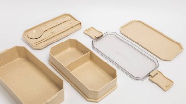 Parçalanmış bento kutusu seti çeşitli bileşenleri içeriyor. İçinde ayırıcı, kaşık, yemek çubuğu ve birden fazla kapak var. Set bronzlaşmış, çevre dostu bir maddeden yapılmış. Görüntü, prodüktörü vurgulayarak beyaz bir arkaplanda çekilmiştir.