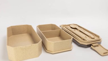 Beyaz arka planda bej bir beslenme çantasının izole edilmiş görüntüsü. Sette bölünmüş bir kap, tek bir kap, kaşık, çubuk ve çatallı bir kapak yer alıyor. Beslenme çantası çevre dostu malzemelerden yapılmıştır ve yemek hazırlığı için mükemmeldir.