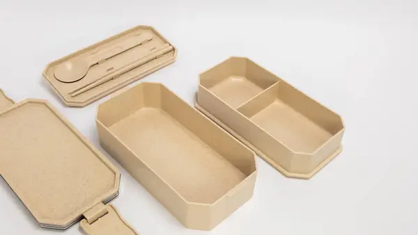 Kapaklı, kaşıklı, çubuklu ve kompartımanlı bej bento seti olan yakın plan bir fotoğraf. Bu çevre dostu yemek konteynırı dayanıklı malzemeden yapılmıştır. Yemek hazırlamak ve yemek paketlemek için mükemmel. Set beyaz arka planda, Highligh