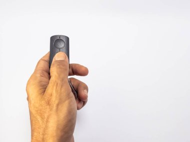 Koyu renkli küçük bir uzaktan kumandayı tutan bir elin yakın çekimi. Uzaktan kumandayı ve onu tutma eylemini vurgulamak için el beyaz bir arkaplana dayanıyor. Güç düğmesi açıkça görülüyor. Görüntü basitliği iletir ve odaklanır