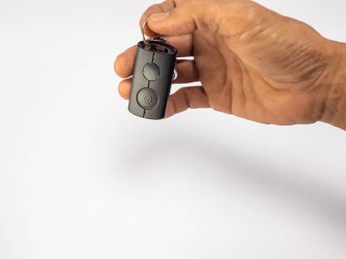 Bir insanın elinde iki düğmesi ve bir güç sembolü olan küçük, siyah bir elektronik cihaz vardır. Cihaz bir anahtarlıkta. El, alttaki yumuşak gölgeyle birlikte düz beyaz bir zemine kurulur. Resim aygıtı ve simülasyonu vurgular