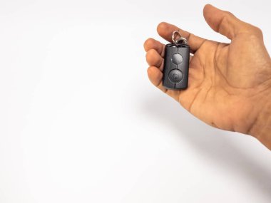 Siyah bir arabanın uzaktan kumandasını temiz beyaz arka planda tutan birinin eli. El, görüntünün sağ üst köşesine yerleştirilir ve geniş bir negatif alan bırakır. Uzaktan kumandada iki düğme ve bir anahtarlık var. Işıklandırma eşit, ve f