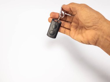 Yakın çekimde, metal bir anahtarlığa bağlı siyah bir arabanın anahtarlığını tutan bir el görülüyor. El, temiz beyaz bir arkaplana dayanır ve basit ve modern bir kompozisyon oluşturur. Görüntü, anahtarlığın ve tutuş eyleminin altını çizer