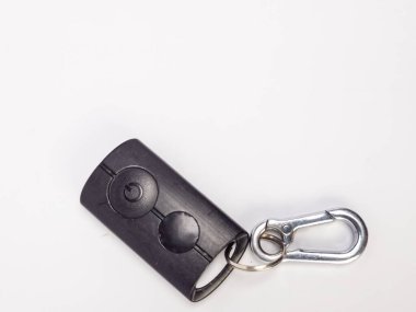 Gümüş bir karabina şarjörüne takılmış siyah bir arabanın yakın çekim çekimi. Fob 'un iki dairesel düğmesi var. Arka plan düz beyaz. Görüntü iyi aydınlatılmış, keskin odaklı ve basit, temiz bir estetik sunuyor. Projec için ideal.