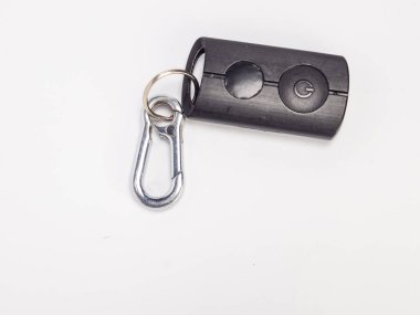 Güç düğmesi ve anahtarlığa takılmış gümüş bir karabina kancasıyla siyah bir anahtarlığın yakın plan çekimi. Anahtarlık beyaz bir yüzeyde yatıyor. Görüntü iyi aydınlatılmış ve anahtarlık ve kancanın detaylarına odaklanmış. Kompozisyon çok basit.