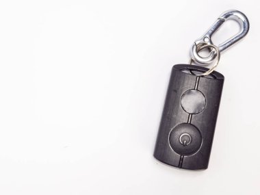 Yakından çekilen bir resimde parlak, siyah bir araba anahtarlığı gümüş bir karabina klipsine tutturulmuş beyaz bir zemin var. Anahtarlıkta iki düğme var, birinde güç sembolü var. Karabina biraz işlevsellik katıyor. Kompozisyon basit.