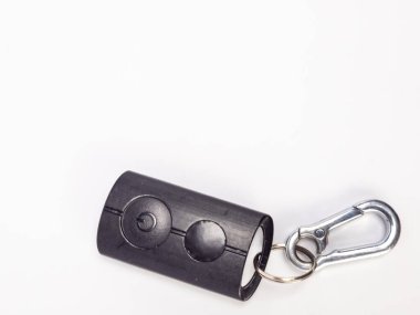 Siyah uzaktan kumandalı, güç düğmesi ve gümüş bir karabina şarjörüne iliştirilmiş başka bir düğmesi olan yakın çekim bir stüdyo fotoğrafı. Kumanda düz beyaz bir arka planda duruyor, temiz ve dağınık bir estetik sunuyor. Teknolojide kullanmak için ideal, Li.