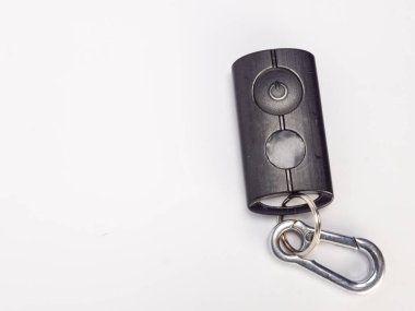 Üzerinde iki düğme ve bir güç sembolü olan siyah bir uzaktan kumandanın yakın çekim görüntüsü. Uzaktan kumanda, beyaz bir yüzeyde duran gümüş bir karabinaya bağlı. Görüntü iyi aydınlatılmış ve minimalist bir stili gösteriyor..