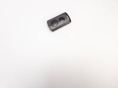 Sade beyaz bir arka planda izole edilmiş modern bir araba anahtarlığının yakın plan, tepeden tırnağa çekimi. Anahtarlık koyu gri renkte ve güç sembolü olan iki düğmesi var. Kompozisyon basit ve temiz, anahtarlığı vurguluyor..