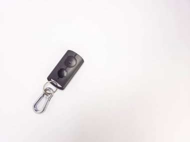 Sade beyaz arka planda gümüş anahtarlığı olan siyah bir araba anahtarının yakın plan çekimi. Anahtarın iki tuşu ve bir güç sembolü var. Görüntü iyi aydınlatılmış, anahtarlık ve anahtarlığa odaklanmış. Bileşimi basit ve temiz, bol negatifli.