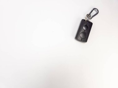 Siyah bir arabanın anahtarlığının gümüş karabinalı yakın plan fotoğrafı. Anahtar anahtarı dikdörtgen, iki düğme ve bir logo. Karabina küçük metal bir yüzüğe bağlı. Arkaplan bembeyaz, temiz ve minimalist bir estetik oluşturuyor..