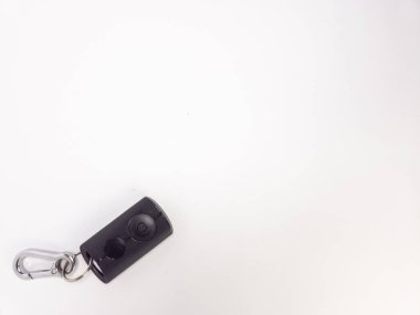 Siyah bir arabanın uzaktan kumandalı gümüş anahtarlığı ile yakın plan görüntüsü. Uzaktan kumandanın güç düğmesi var. Anahtar, ticari kullanım için geniş bir kopya alanı sağlayan temiz beyaz bir arkaplanda izole edilmiş. Kompozisyon basit, temiz ve modern..