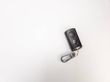 Temiz beyaz bir yüzeye bağlı bir karabinayla siyah bir uzaktan kumandanın yakın çekim çekimi. Uzaktan kumandada iki düğme var, birinde güç sembolü var. Karabina gümüş renktedir ve küçük metal bir halkayla uzaktan kumandaya bağlanır. İma.