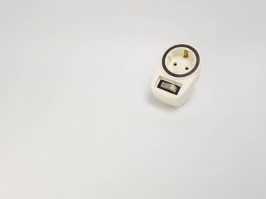 Yüksek açılı bir çekim, temiz beyaz arka plana karşı açılı ve açma kapama düğmesi olan krem renkli bir elektrik adaptörünü gösterir. Adaptörün tasarımı bir güç çıkışı ve bir anahtar içeriyor. Bu da elektriksel işlevsellik ve güvenliği gösteriyor. Ne?