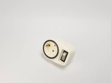 Yakın çekim bir stüdyo çekiminde beyaz bir elektrik adaptörü ve dahili açma kapama düğmesi bulunur. Adaptör, temiz tasarımı ve işlevselliğini vurgulayarak kusursuz beyaz bir arkaplan üzerine kurulmuştur. Resim adaptörün pratik kullanımını vurgular.