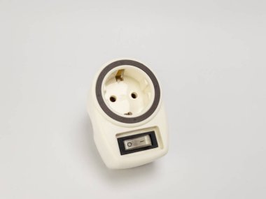 Dahili açma kapama düğmesi olan beyaz bir elektrik prizi adaptörünün yakın çekim görüntüsü. Adaptör, temiz ve beyaz bir arkaplana karşı köşegen olarak konumlandırılmış. Görüntü, buji reçelini gösteren adaptörün tasarımı ve işlevselliğini vurgular