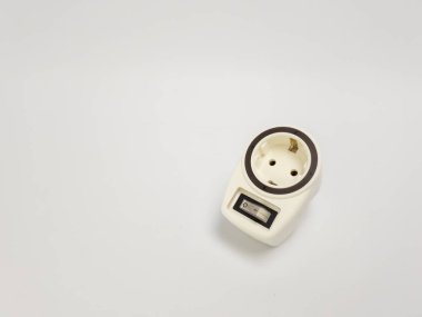 Kapatma düğmeli beyaz bir elektrik prizi adaptörünün yakın çekim görüntüsü. Adaptör, tasarımı ve işlevselliğini vurgulayan düz beyaz bir arkaplana göre ayarlanır. Resim, p ile ilgili çeşitli kullanımlar için uygun yaygın bir ev ögesini gösterir