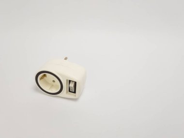 Beyaz bir elektrik adaptörünün yakın plan çekimi. Elektrik prizi ve temiz beyaz bir arkaplan karşısında açma kapama düğmesi. Adaptörün işlevselliğini vurgulayan basit bir tasarımı var. Görüntü ürünün detaylarına odaklanarak iyi aydınlatılmış..