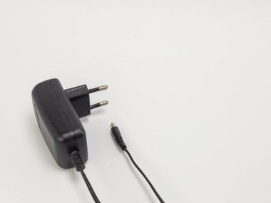 Avrupa prizli bir siyah güç adaptörünün yakın çekim görüntüsü ve küçük bir bağlantıyla ayrı bir kablo. Adaptör beyaz bir yüzeye yerleştirilmiş, bu da temiz ve minimalist bir bileşim olduğunu gösteriyor. Nesnenin kendisi üzerinde duruluyor. 